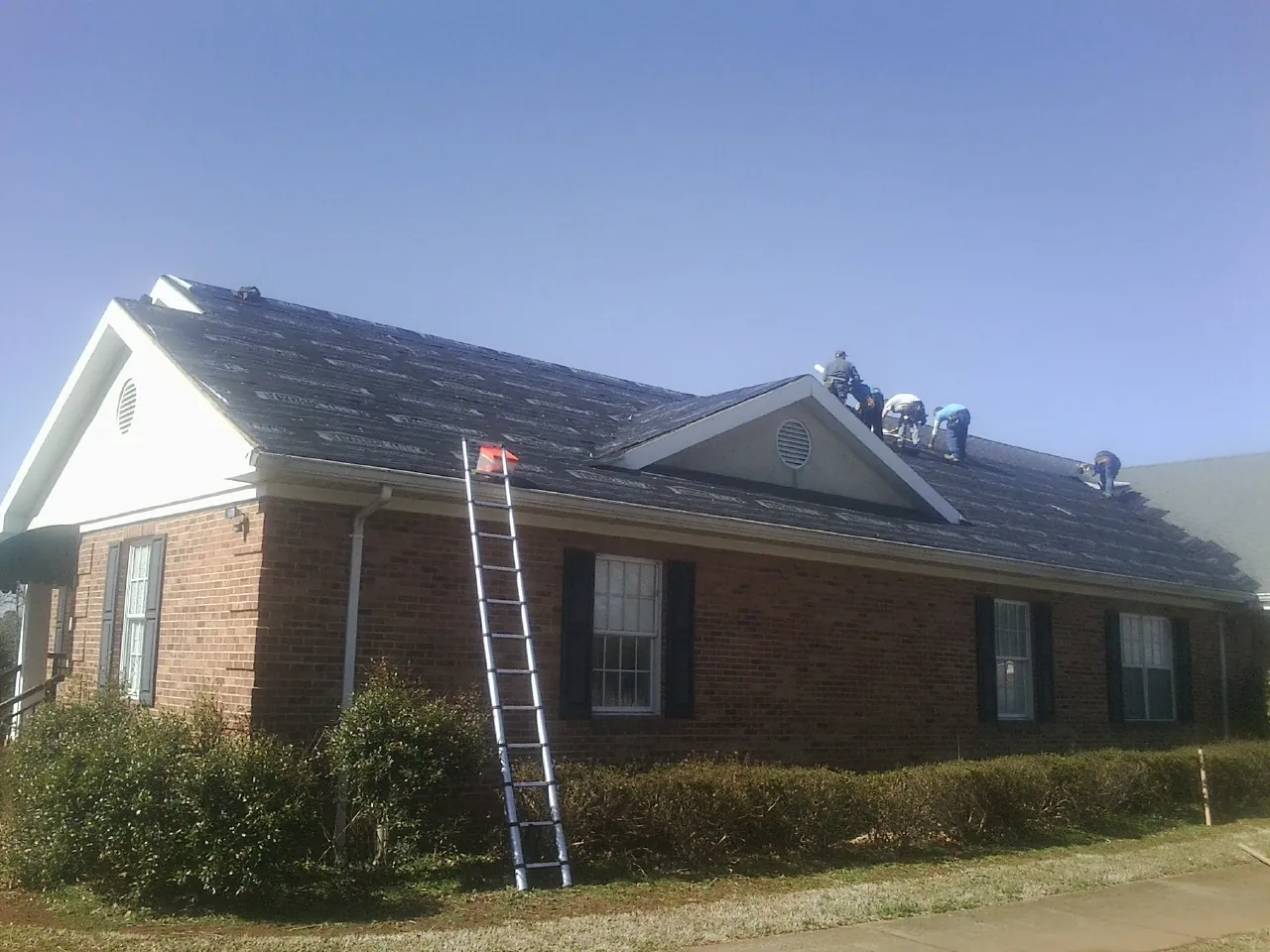 Crew tearing shingles off a brick ranch roof with a ladder set — Emergency Roof Repair work by our crew in Scarville