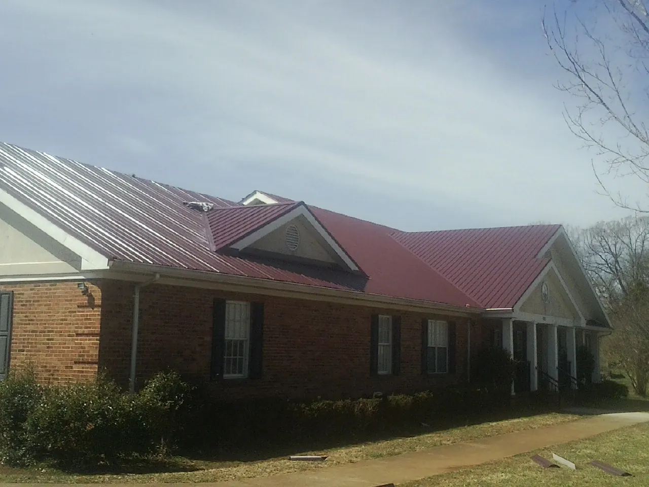 Red metal roof with gabled entries on a long brick building, from a Hail Damage Roof Repair job in Scarville