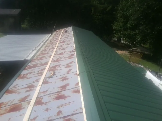 Old rusted panels beside newly installed green metal roofing — Wind Damage Roof Repair by Roofing Brothers in Scarville