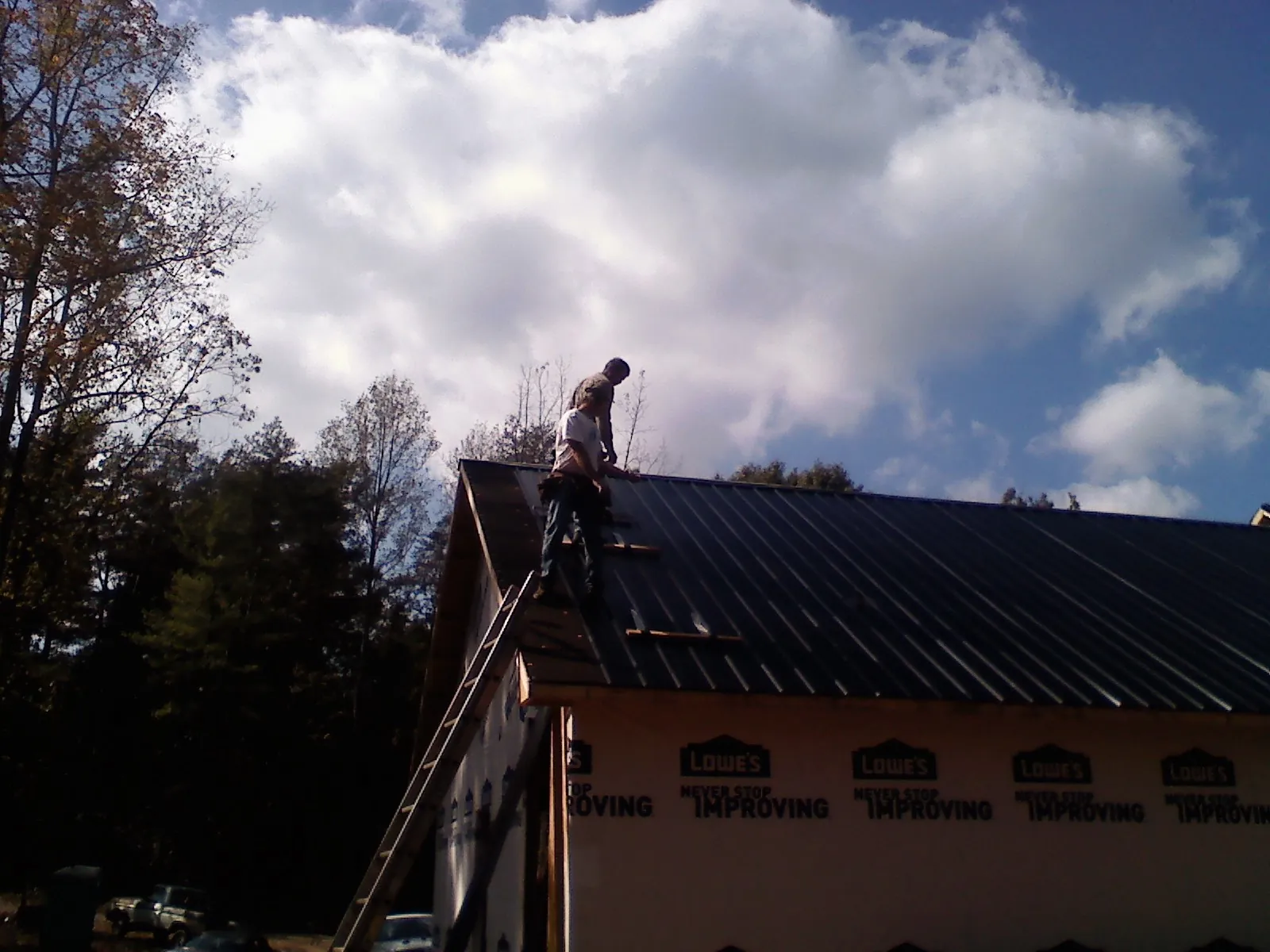 Roofer fastening dark metal panels high against a cloudy sky, from a Roof Inspection job in Scarville