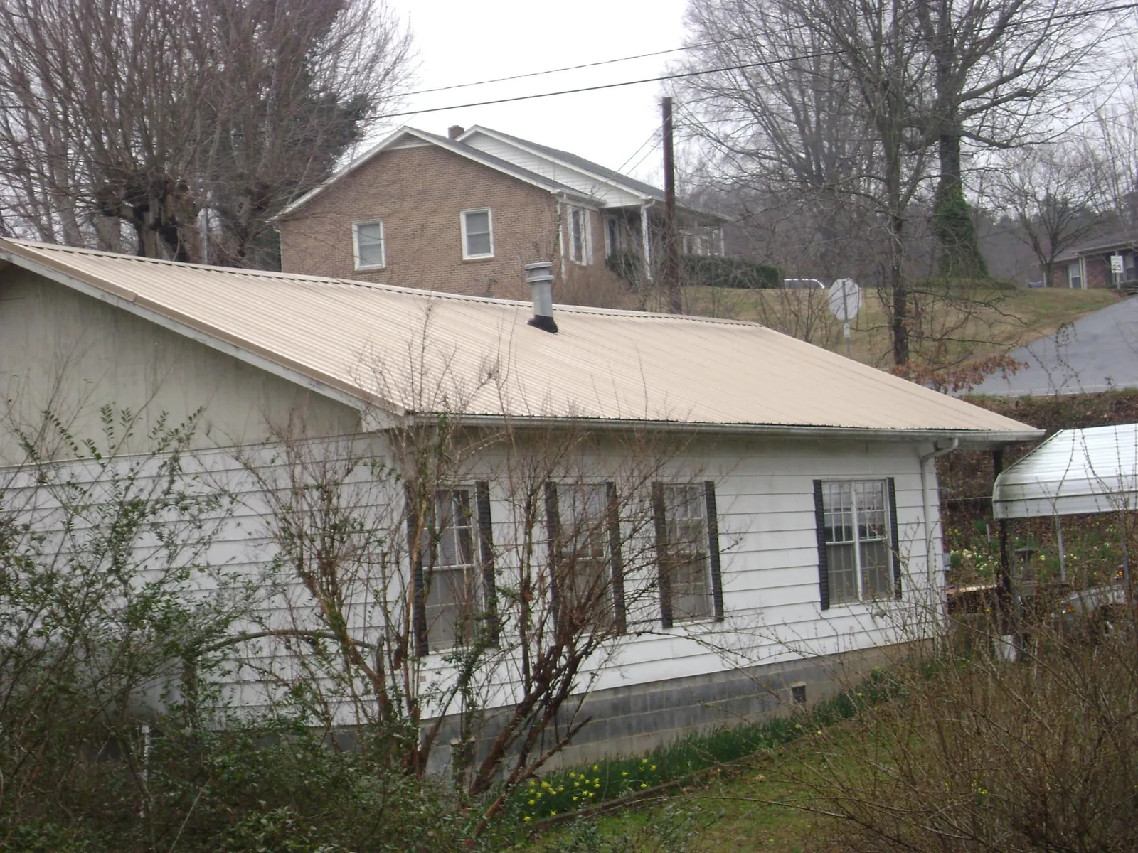 Tan metal roof on a white sided house set into a hillside — Commercial Roofing by Roofing Brothers in Scarville